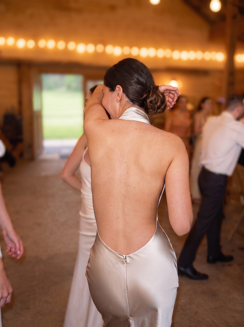 Woman dancing at a wedding in a champagne halter-neck dress, bare back with no bra straps showing