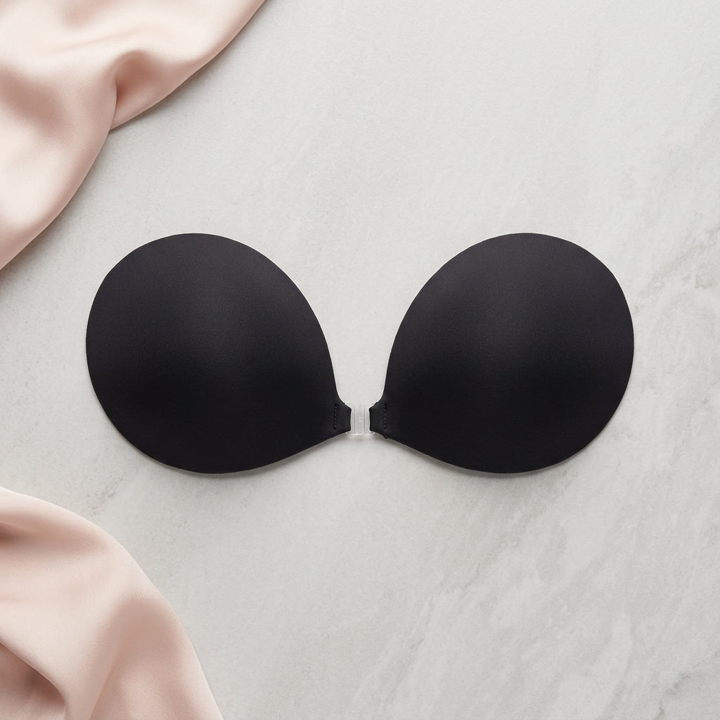 Black adhesive bra pads on a light gray surface with pink fabric.